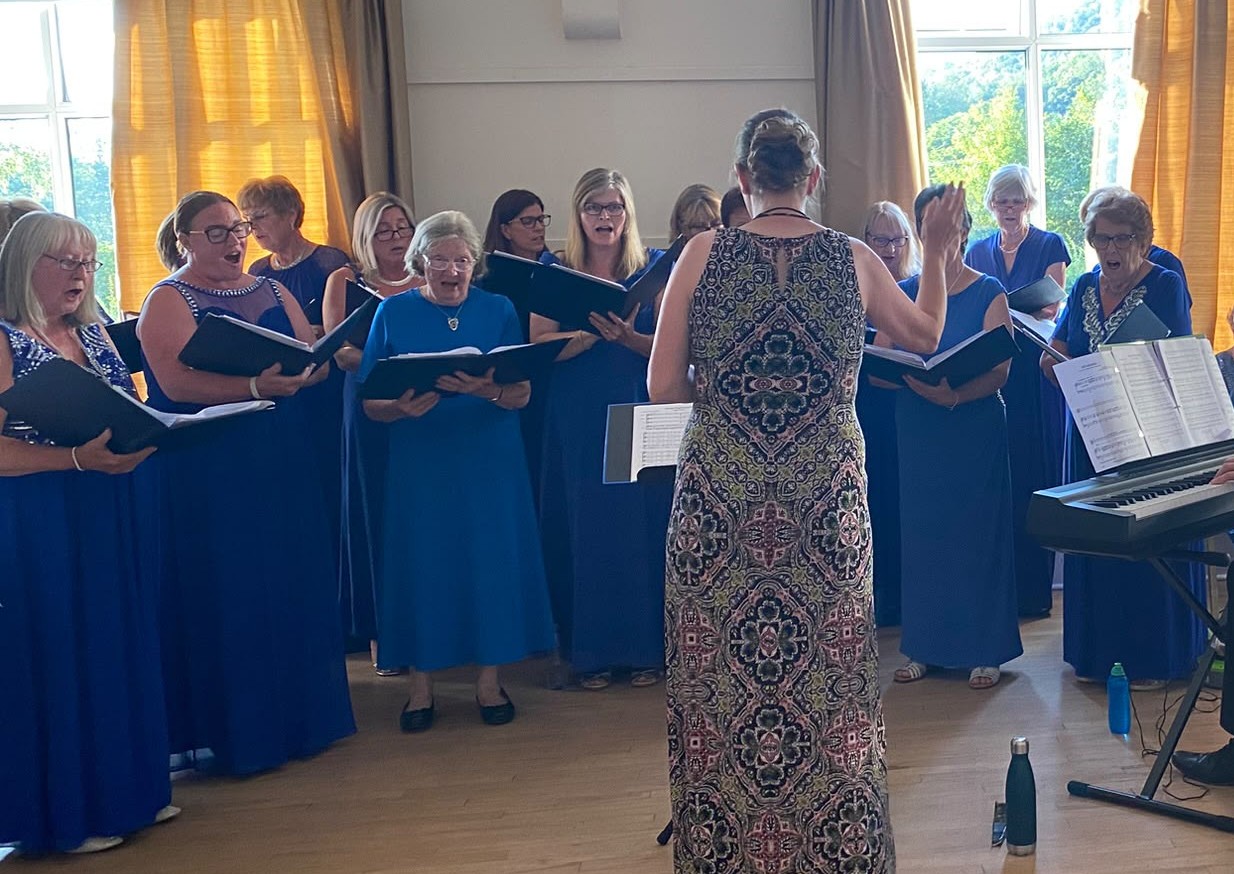 One Achord choir members in blue dresses singing together, led by their conductor.